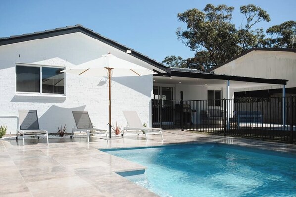 Une maison moderne dotée d’une piscine, d’une façade blanche et d’un patio couvert.