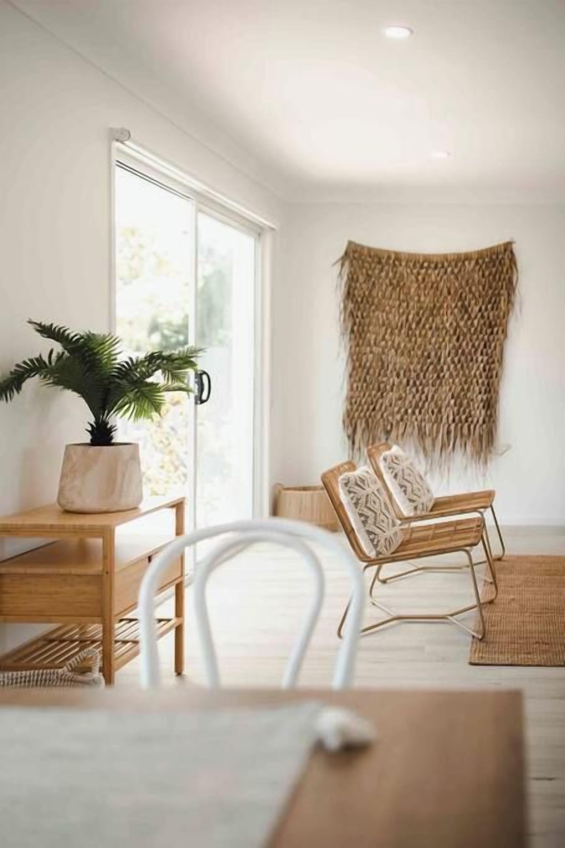 A room with a wooden table, white chairs, a woven wall hanging, and a potted plant.