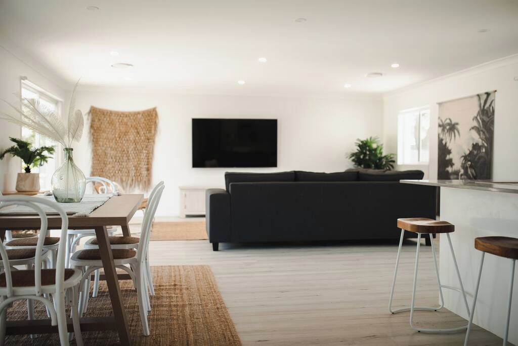 Un salon moderne comprenant un canapé, une table à manger avec des chaises, un téléviseur fixé au mur et une plante.