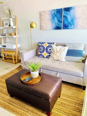 A living room with a sofa, a coffee table with a plant, a bookshelf, and a wall-mounted painting. - Sugar Sands - Ocean front at Symphony Beach Club ! (Ormond Beach)