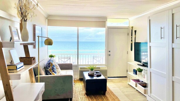 A room with a view of the ocean, a ceiling fan, a sofa, a coffee table, and a TV on a stand. - Sugar Sands - Ocean front at Symphony Beach Club ! (Ormond Beach)
