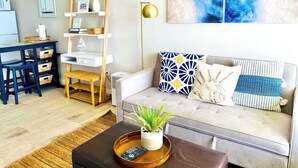 A living room with a sofa, a coffee table with a plant, a bookshelf, a dining area with a table and chairs, and a ceiling fan. - Sugar Sands - Ocean front at Symphony Beach Club ! (Ormond Beach)