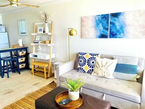 Una sala de estar con sofá, una mesa de centro con una planta, una estantería, una zona de comedor con mesa y sillas, y un ventilador de techo.