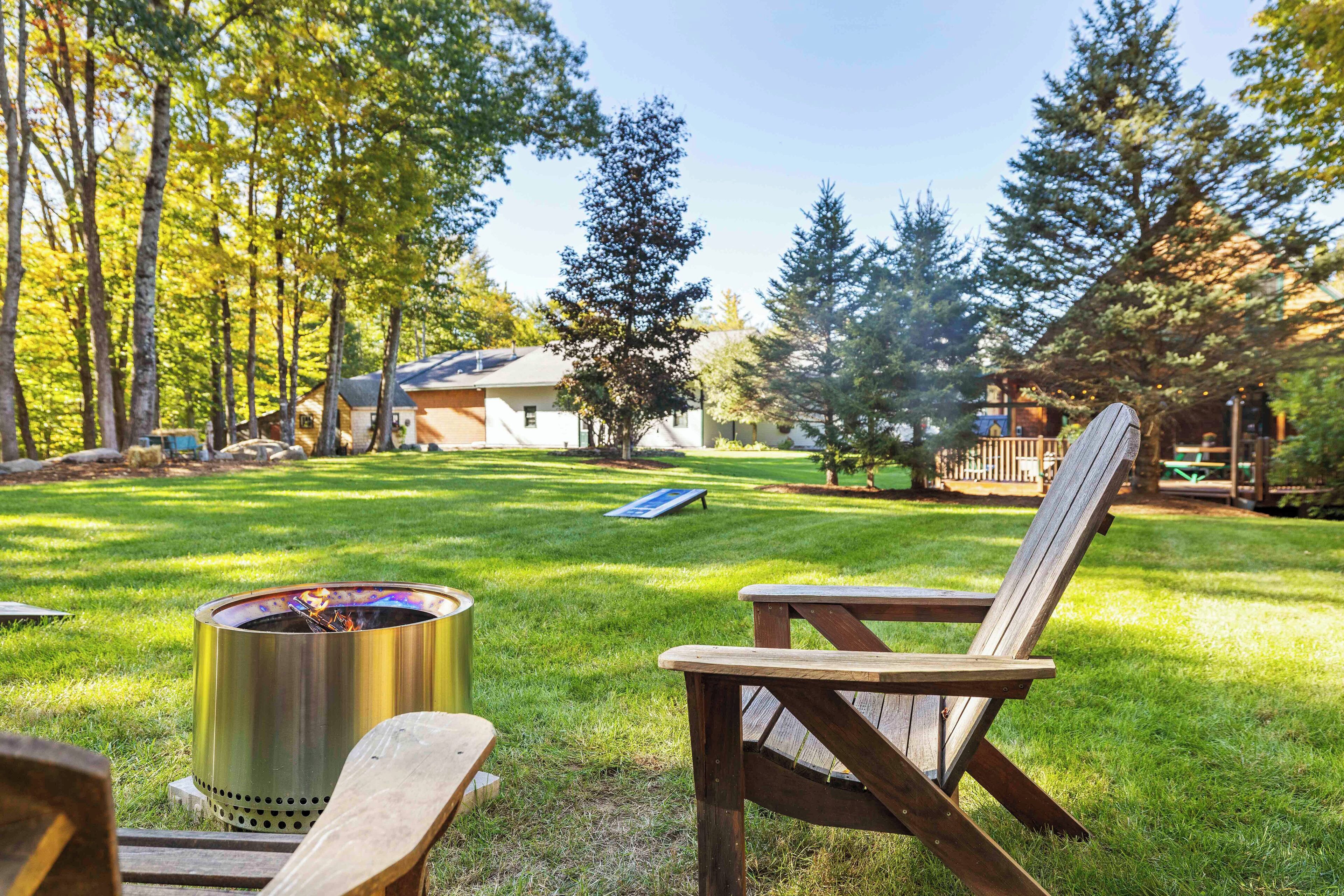 A backyard with a fire pit, wooden chairs, and a grassy lawn.