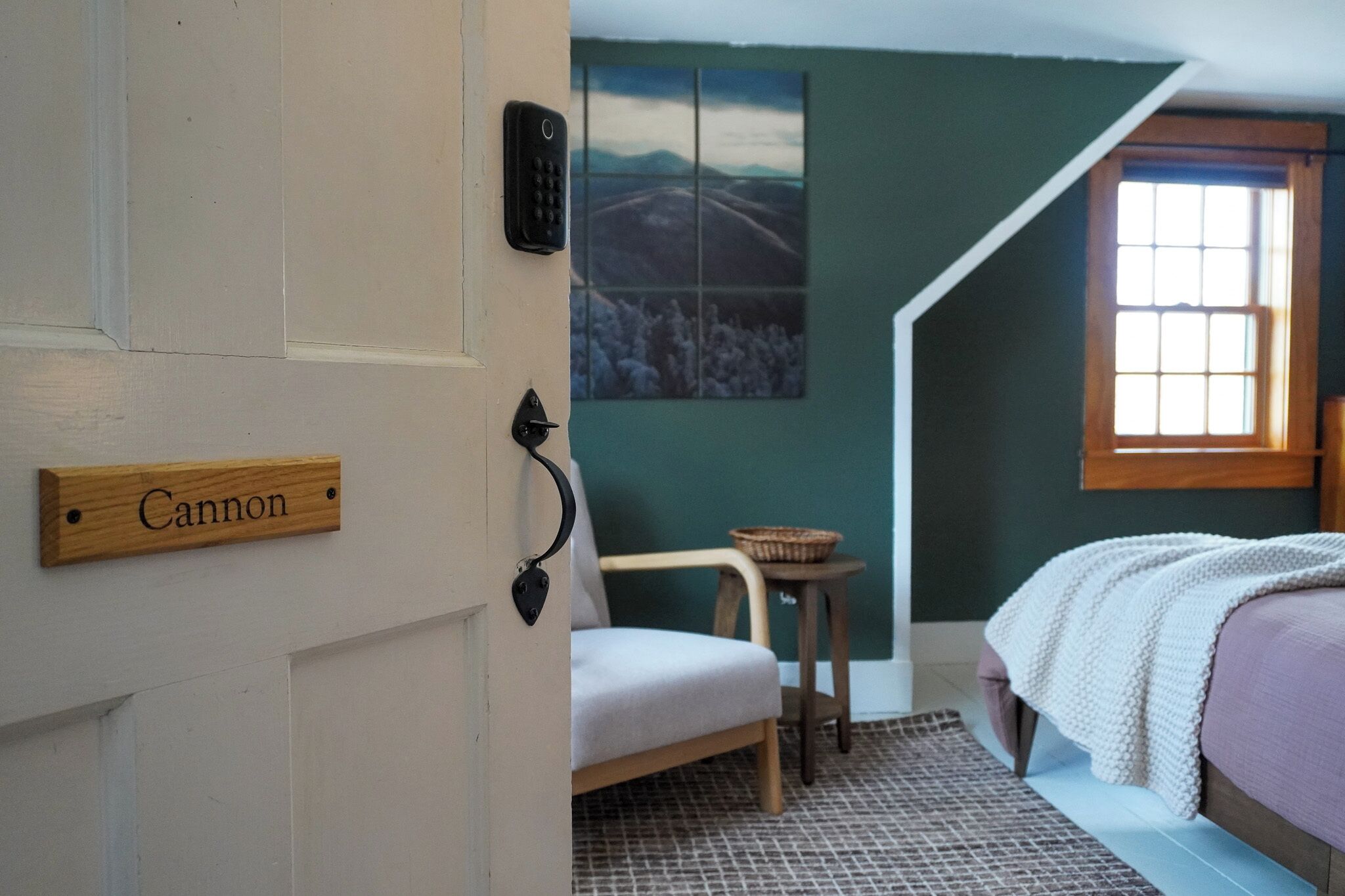Ein Schlafzimmer mit einem Bett, einem Sessel, einem kleinen Tisch, einem Fenster und einer Tür mit der Aufschrift 'Cannon'.