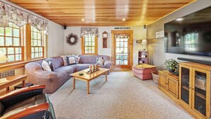 Una sala de estar acogedora con techo de madera, un televisor grande, un sofá, una mesa de centro y una chimenea.