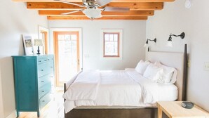 Une chambre à coucher comprenant un lit, une commode, un ventilateur de plafond et une table de chevet.