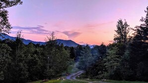 Un feu de camp dans une zone boisée, sous un ciel dégagé, avec des montagnes en arrière-plan.
