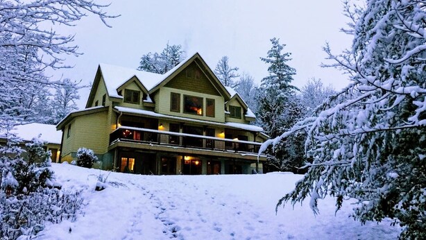 Un grand chalet à plusieurs étages, doté d’un balcon imposant et surplombant un paysage enneigé.