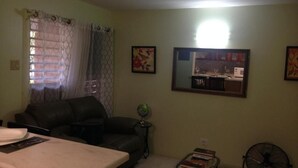 A living room with a sofa, a dining table, a small side table with a globe, and a fan. - Oxford manner Our Gem  (Kingston)