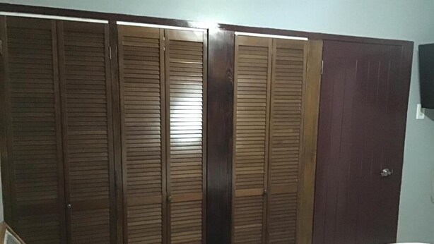 A bedroom with a bed, a wooden wardrobe, and a door. - Oxford manner Our Gem  (Kingston)