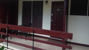A building with a red door marked with the number 61, a covered porch area with a bench, and a potted plant. - Oxford manner Our Gem  (Kingston)
