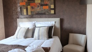 A neatly made bed with pillows and a blanket, a chair, and a wall with a colorful abstract painting. - A break for two in a detached villa with SPA (Sainte-Anastasie)