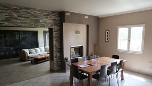 A modern living room with a fireplace, a dining area with a wooden table and chairs, and a large window providing natural light. - A break for two in a detached villa with SPA (Sainte-Anastasie)