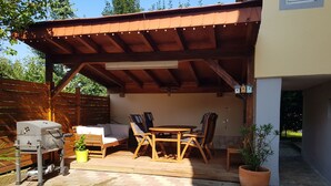 Un patio al aire libre con mesa y sillas de madera, una parrilla y plantas en macetas.