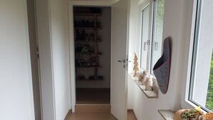 Un pasillo con suelo de madera, un zapatero y una ventana con vistas a la vegetación.