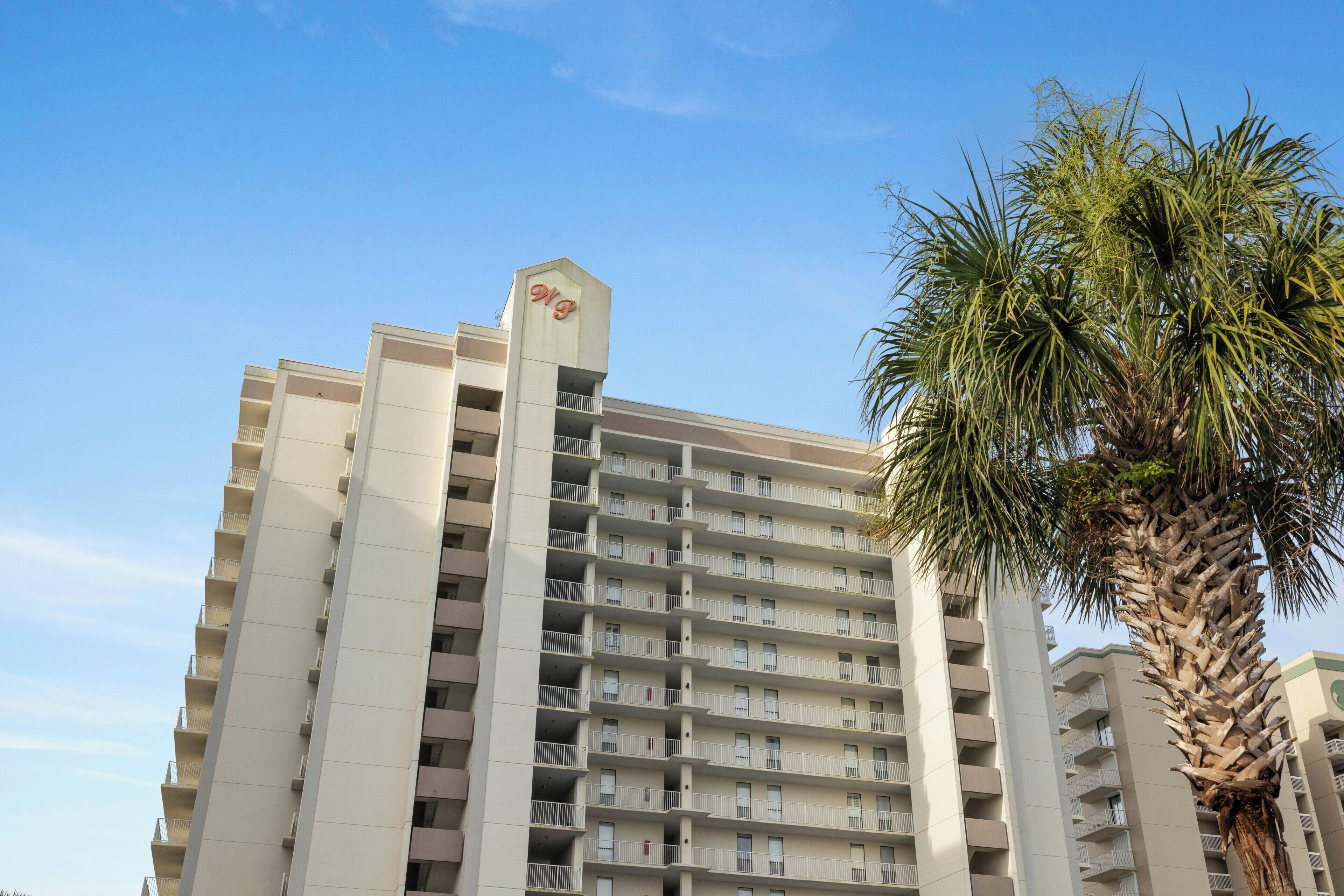 A high-rise hotel with multiple balconies and a palm tree in the foreground.