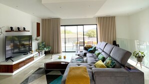 A modern living room with a large grey sofa, a flat-screen TV, and a dining area with a table and chairs. - Magnificent villa with private pool (monticello)