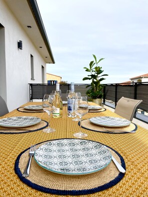 Un área de comedor al aire libre con una mesa preparada para cuatro personas, con platos estampados y un mantel amarillo.