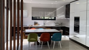 A modern kitchen with white cabinets, a central island with colorful chairs, and a window with a view. - Magnificent villa with private pool (monticello)