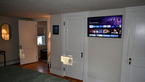 Une chambre à coucher avec un lit, un téléviseur fixé au mur qui diffuse différents services de streaming, et une porte donnant sur une autre pièce.
