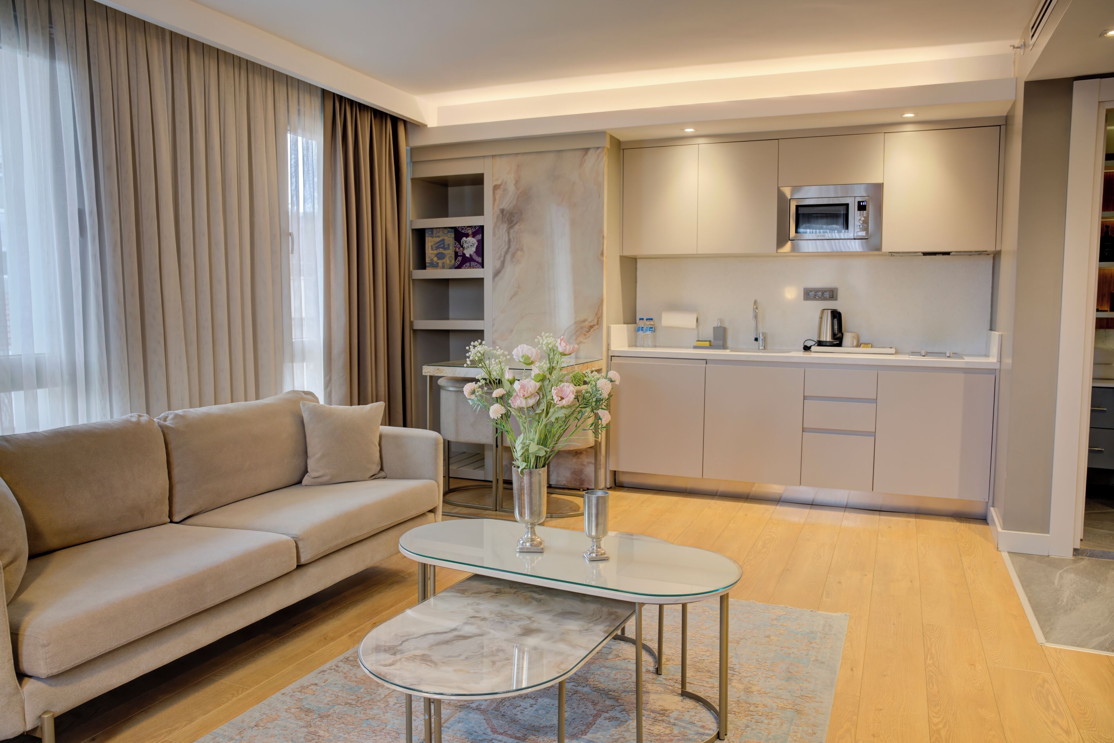 A modern living room with a sofa, a glass coffee table, and a kitchen area with a microwave.