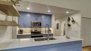 Una cocina moderna con armarios azules, electrodomésticos de acero inoxidable y encimera blanca.