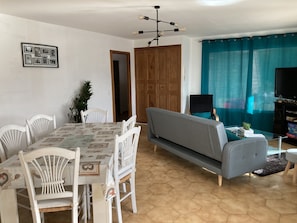 Un coin repas avec une table et des chaises, un canapé, un téléviseur et une porte donnant sur une autre pièce.