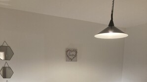 A bedroom with a wooden headboard, two beds with matching pillows, a wall-mounted mirror, a decorative heart-shaped sign, and a hanging pendant light.