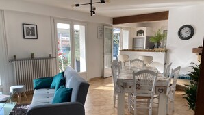 A modern living room with a grey sofa, a dining table with white chairs, and a kitchen area in the background.