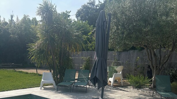 A swimming pool with clear water, surrounded by a patio area with chairs and an umbrella.