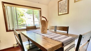 Un coin repas avec une table en bois, des bancs, un ventilateur de plafond et une fenêtre avec des rideaux.