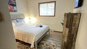 Une chambre à coucher comprenant un lit, une armoire en bois, un téléviseur et une fenêtre avec des stores.