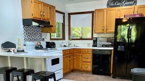 Une cuisine moderne avec des meubles en bois, un réfrigérateur noir, une cuisinière blanche et un coin bar avec des tabourets.