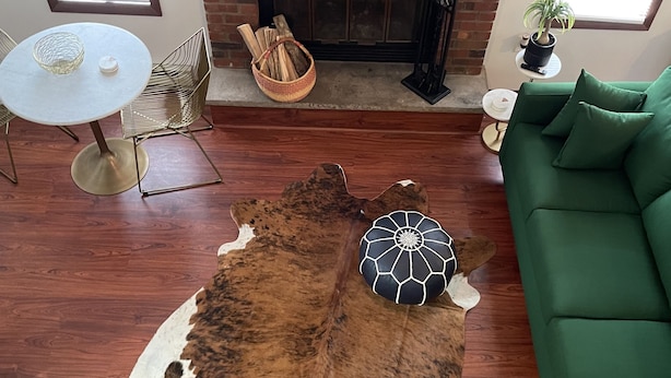 Un salon avec un canapé vert, une table ronde, un tapis en cuir et une cheminée.
