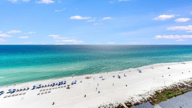 A beach with clear blue water, white sand, and a few umbrellas.