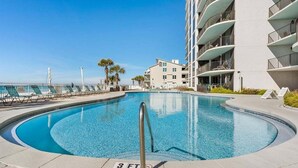 A swimming pool with a 3 ft depth marker, surrounded by lounge chairs and a building with balconies.