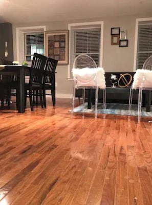 A dining area with a wooden floor, a black dining table, and chairs. There are two windows with blinds, and a small globe decoration on the wall.