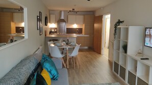 A modern living room with a sofa, a dining area with a table and chairs, a kitchen with cabinets and a range hood, and a TV on a shelf. - Fantastic Centrally Located 1 bed Apartment (Liverpool)