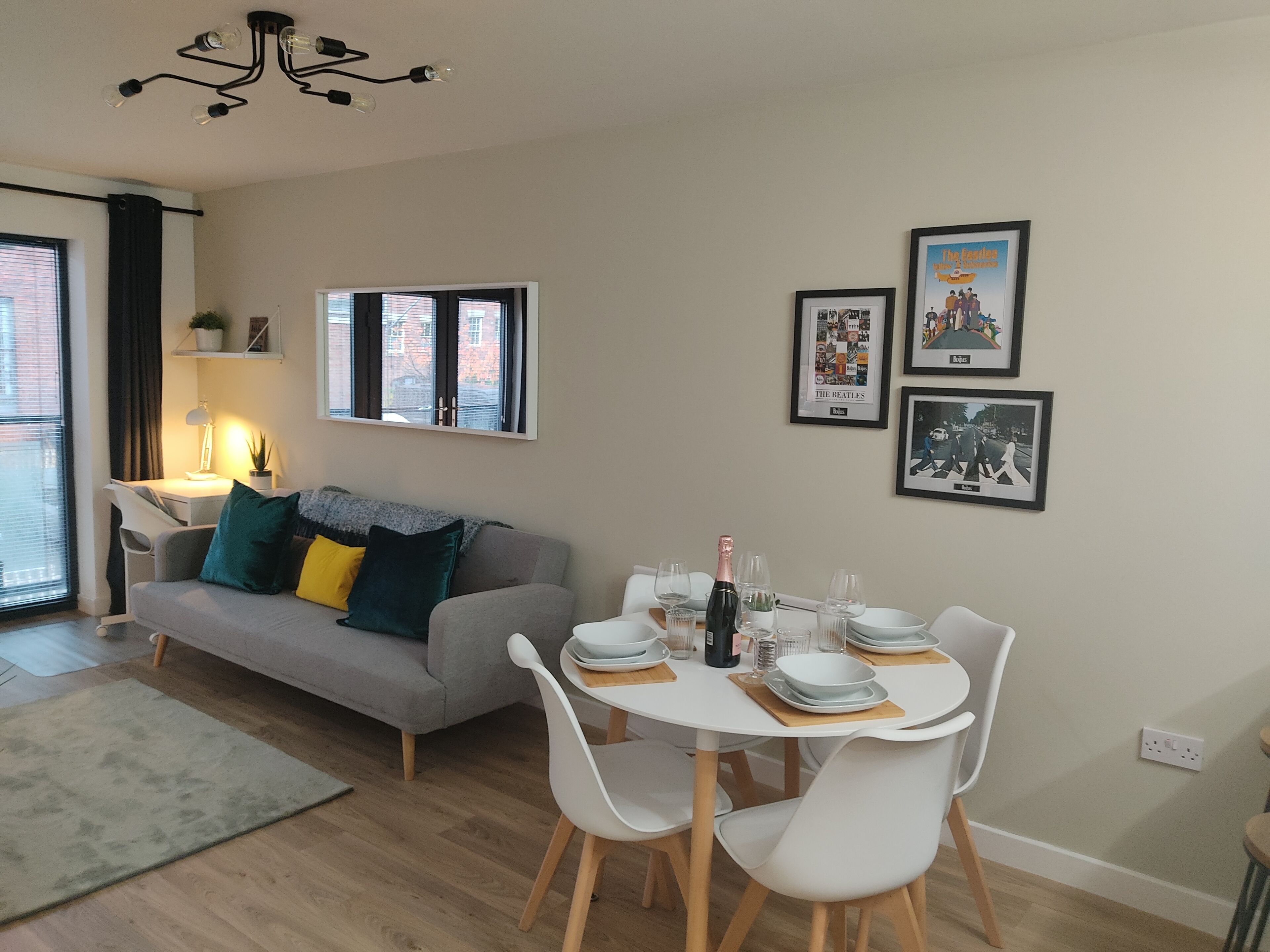 Ein modernes Wohnzimmer mit Essbereich, einer Couch mit Kissen, einem Tisch für zwei Personen und gerahmten Bildern an der Wand.
