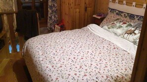 A bedroom with a floral-patterned bedspread, wooden walls, and a window with lace curtains. - Monterosa winter vacation home (Gressonay Saint Jean)