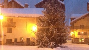 A snow-covered courtyard with a snow-covered tree and buildings in the background. - Monterosa winter vacation home (Gressonay Saint Jean)