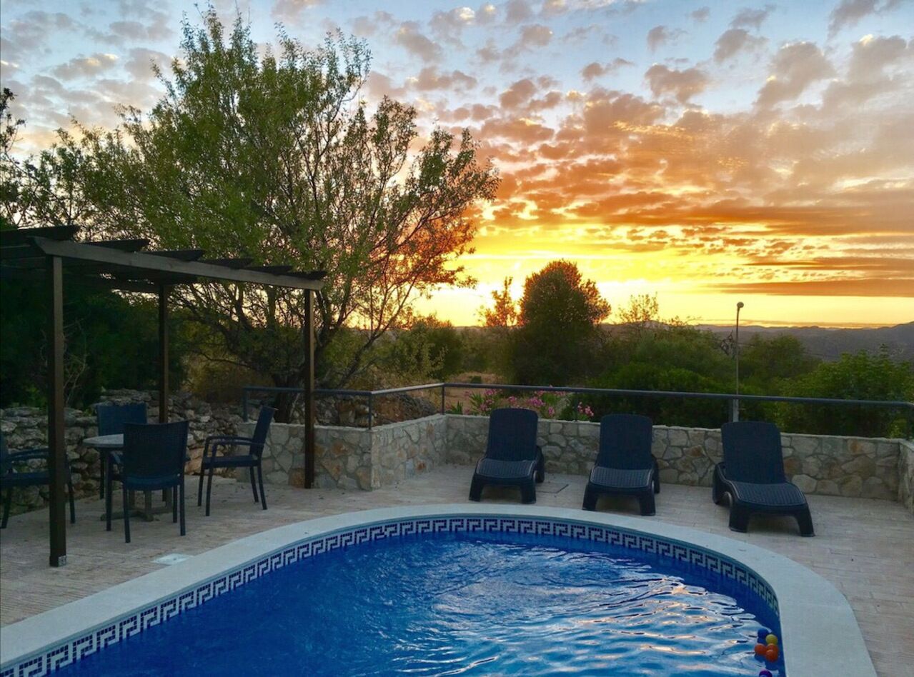 A pool with a geometric tile pattern, surrounded by lounge chairs and a pergola.