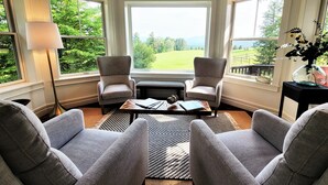 A room with two armchairs, a coffee table, and a view of a green landscape through large windows.