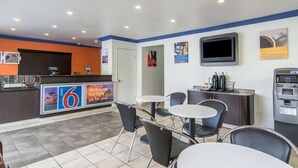A hotel lobby with a reception desk, a TV, a coffee machine, and seating area. - Beachside Inn (Anaheim)