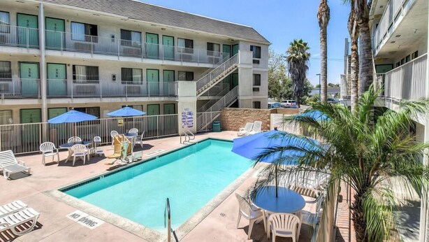 A hotel with a swimming pool, outdoor seating, and palm trees. - Beachside Inn (Anaheim)
