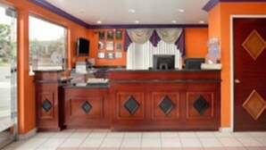 A reception area with a wooden counter, a television, and a window with curtains. - Beachside Inn (Anaheim)