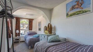 A bedroom with two beds, a window with curtains, a desk, and a painting on the wall. - Charming Old Town Cottage With Modern Features (Hastings)