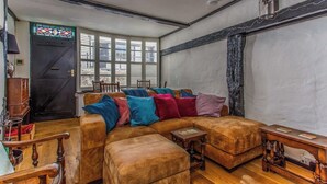 A cozy living room with a brown leather sofa, colorful cushions, a wooden coffee table, and a stained glass window. - Charming Old Town Cottage With Modern Features (Hastings)