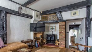 A cozy living room with a fireplace, a television, and wooden furniture. - Charming Old Town Cottage With Modern Features (Hastings)